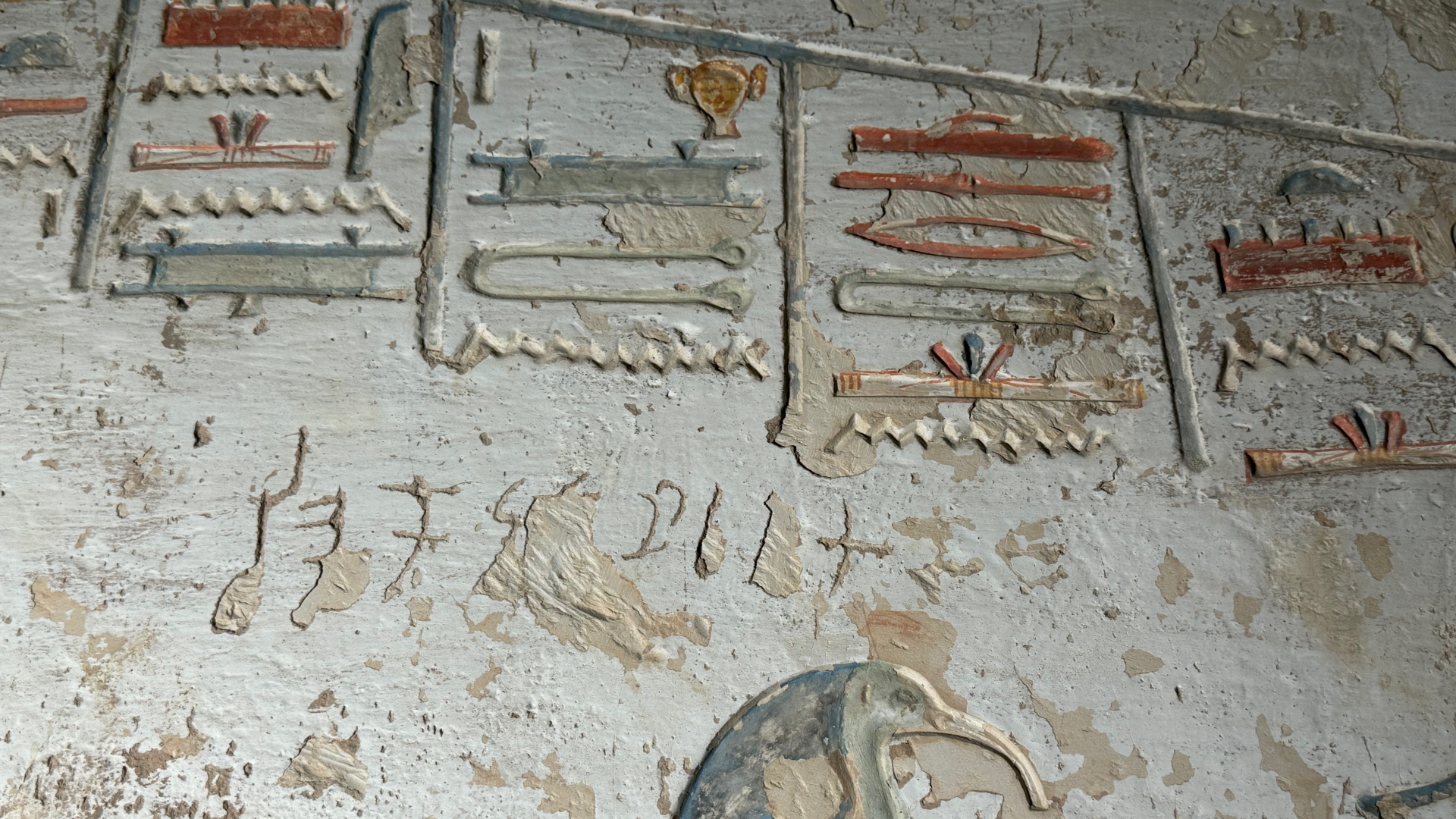 A white wall shows golden and blue heiroglyphs along with small letters carved into the wall