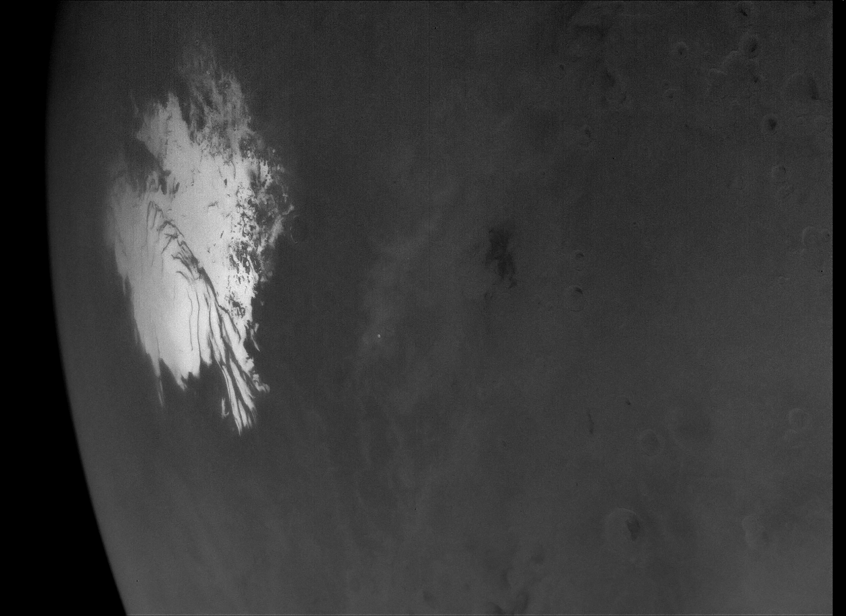 A close-up, greyscale image of the Martian surface, highlighting the intricate, swirling edges and dark troughs of a bright white polar ice cap next to surrounding plains textured with faint craters.