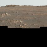 Perseverance poslal selfie z najzápadnejšieho okraja svojej marsovskej trasy Undulating terrain of reddish-brown soil and loose rocks stretches toward a rugged horizon. The sky above is hazy and pale. The image’s bottom edge is a jagged black border, indicating the edges of the frames stitched together to create the mosaic.