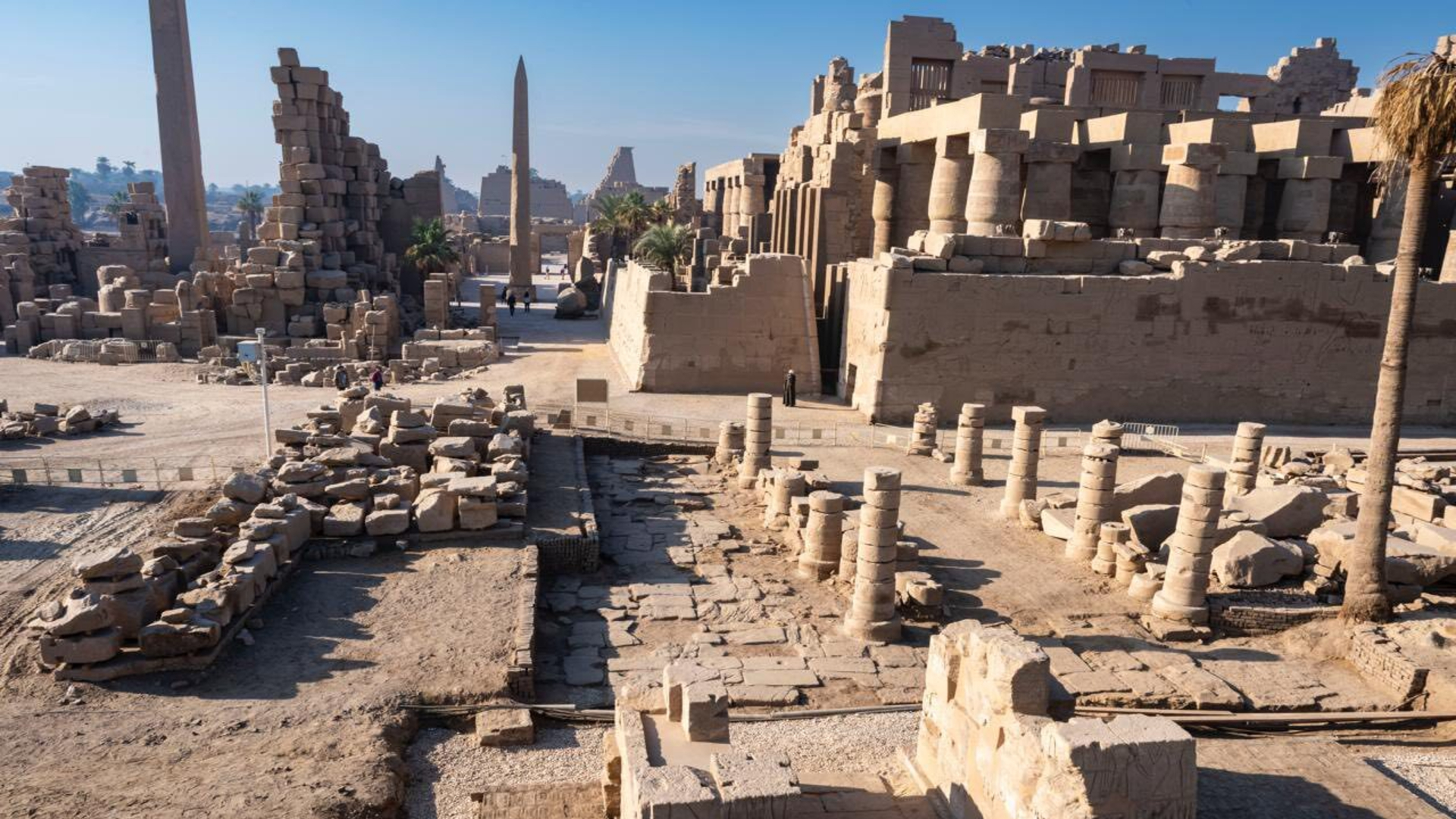Photos from an archaeological dig, showing a brown stone tablet with hieroglyphics written on it, a group of people standing around the tablet, and a shot of the ruins of an ancient city