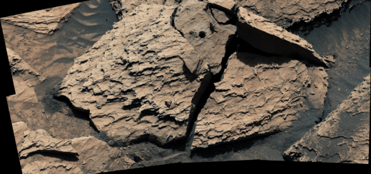 A large, reddish-brown rock as seen by NASA's Curiosity Mars rover. The rock is broken into several pieces. A drill hole is visible in the top middle piece.