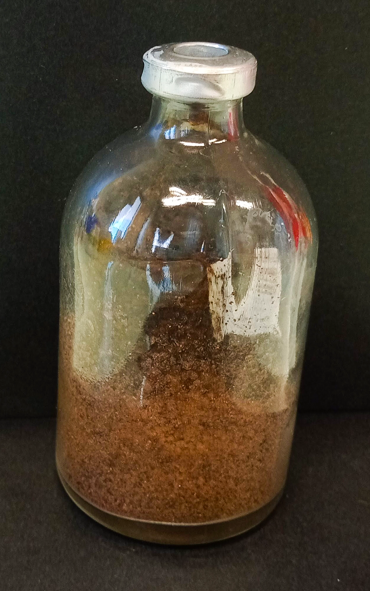 A glass jar filled one-third of the way with dirt.