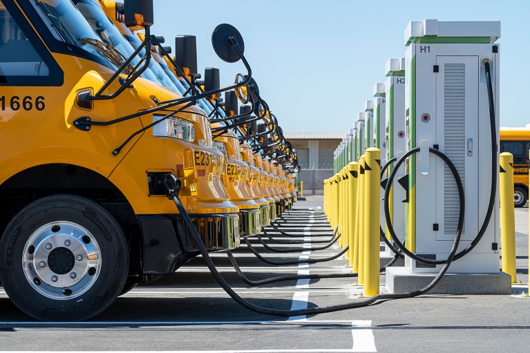 A line of yellow electric school buses in the USA, connected to their charging stations.