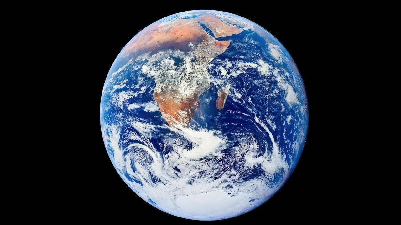 A blue and white sphere with brown continents on it is seen in the darkness of space.