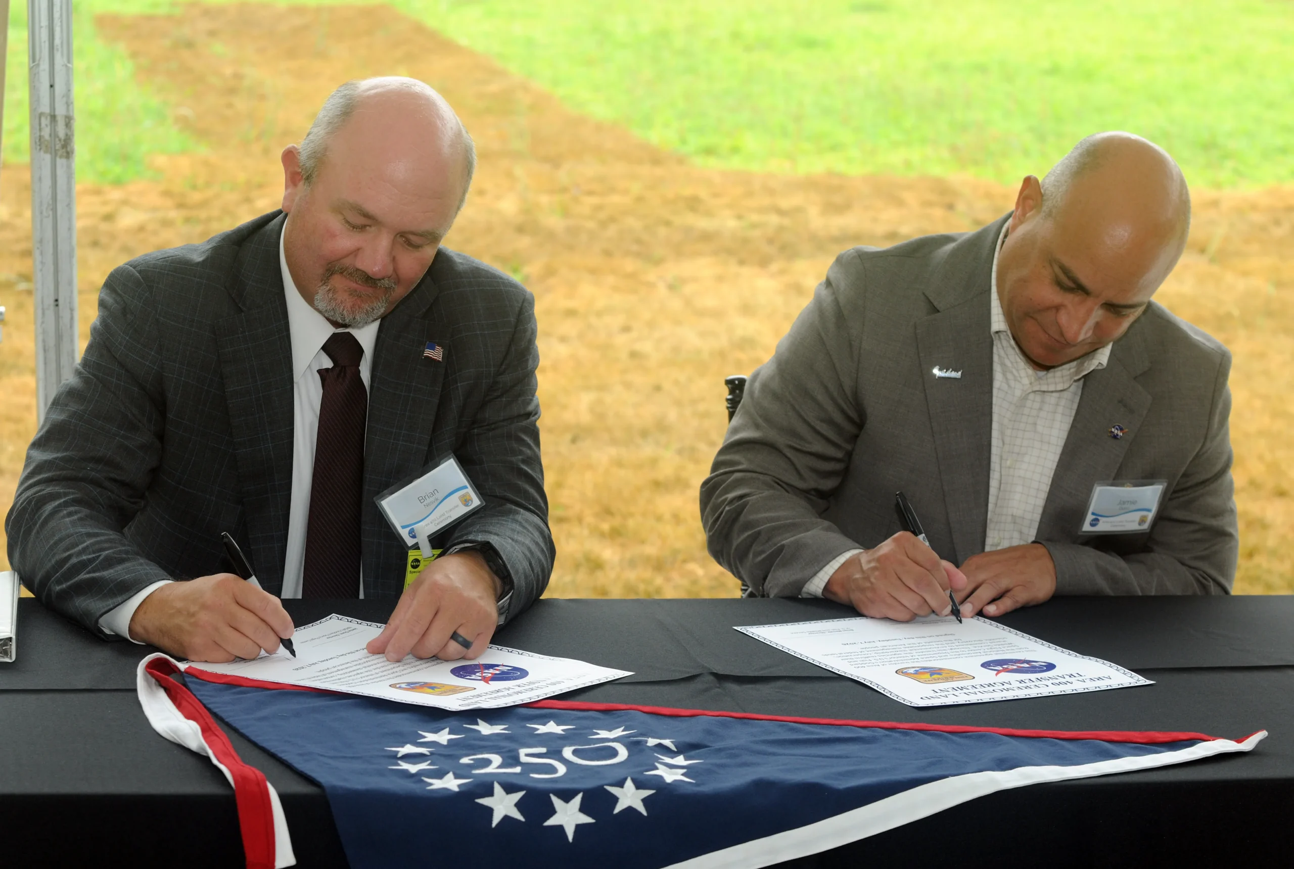 two men sign certificates on a table with black tablecloth