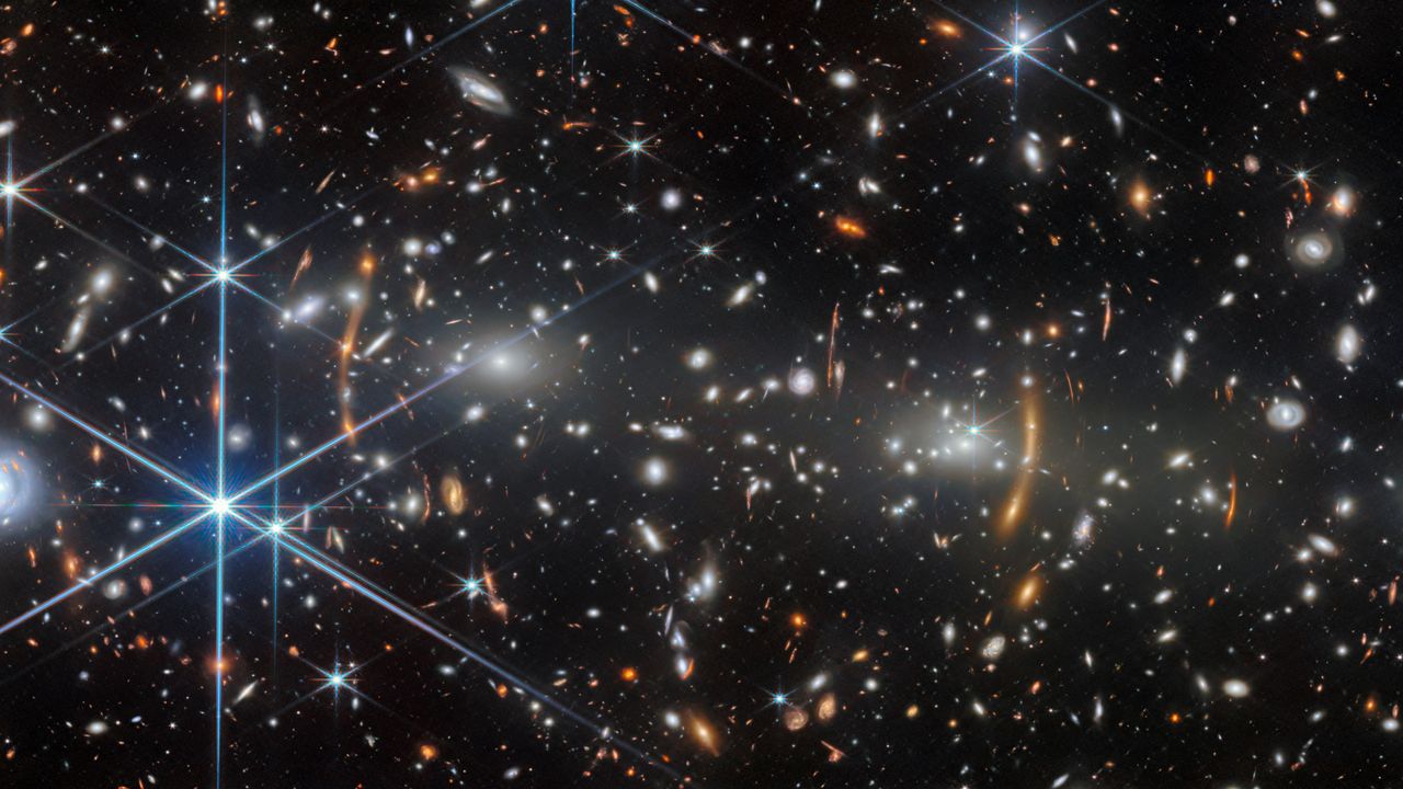 A deep field image of the universe with orange blurs showing gravitationally lensed objects